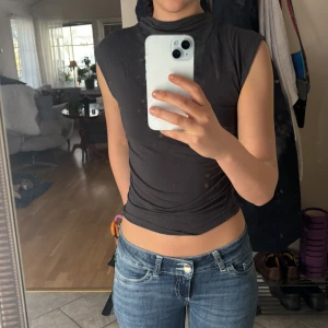 Mörkgrå ärmlös topp från Gina tricot - Säljer en snygg ärmlös topp från Gina tricot. Toppen har en hög krage och en tight passform. Perfekt för att matcha med jeans eller kjol för en enkel men snygg look. Säljer pga att den inte kmr till användning🩶