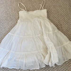 Vit klänning från Gina Tricot - Söt vit klänning från Gina Tricot med smala axelband och volangdetaljer. Perfekt för varma sommardagar. Klänningen har en luftig och lätt design som ger en romantisk känsla.