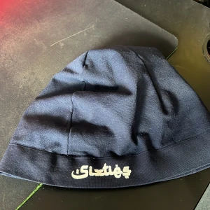 Mörkblå sixties mössa - Snygg mörkblå mössa med vit broderad text framtill. Perfekt för kyliga dagar och en stilren look. Tillverkad i ett mjukt material som sitter bekvämt på huvudet.