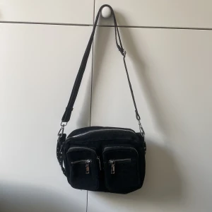 Svart axelväska med dragkedjor - Snygg svart axelväska med flera dragkedjor och justerbar axelrem. Väskan har två framfickor med dragkedja och en huvudficka med dragkedja. Perfekt för att hålla dina saker organiserade och lättillgängliga.Aldrig använd.