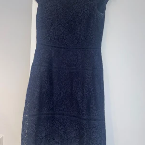 Marinblå spetsklänning - Elegant mörkblå klänning i spets med korta ärmar. Perfekt för en stilren look med vackra detaljer och en feminin siluett.