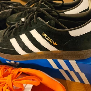 Adidas Spezial svarta sneakers - Svarta Adidas Spezial sneakers med vita ränder och gummisula. Skon har snörning och är tillverkad i mocka med detaljer i vitt och guldtext på sidan. Klassisk och stilren modell som passar till mycket.