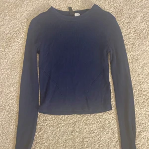 Mörkblå magtröja - Säljer en mörkblå långärmad tröja med ribbad struktur och croppad passform. Perfekt för dig som gillar en enkel men trendig stil. Tröjan har rund halsringning och är mjuk och skön att bära.