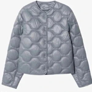 Ljusgrå quiltad jacka från Uniqlo - Säljer en ljusgrå quiltad jacka från Uniqlo med rund halsringning och tryckknappar framtill. Jackan har ett unikt vågigt quiltmönster och är lätt vadderad, perfekt för lager-på-lager under höst och vår.
