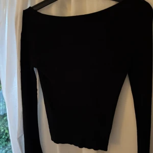 Svart ribbad långärmad topp - En svart, ribbad långärmad topp med bred urringning där bak. Toppen är tight i passformen och har en enkel, stilren design som passar till många olika outfits.