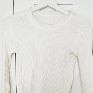 Vit ribbad långärmad tröja - Säljer en enkel och stilren vit ribbad tröja med lång ärm. Perfekt basplagg som passar till många olika outfits. Tröjan har rund halsringning och är figurnära i modellen.