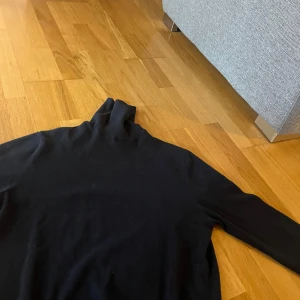 Svart polotröja från Springfield - Svart polotröja från Springfield i storlek M. Tröjan har lång ärm och hög krage, perfekt för lager-på-lager eller som den är. Enkel och stilren design som passar till mycket.