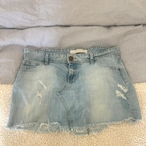 jeanskjol - Säljer en ljusblå jeanskjol med slitna detaljer och fransad nederkant. Kjolen har klassisk femficksdesign och knappstängning framtill. Perfekt till sommaren! Midjemått: 78 cm | aldrig använd
