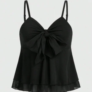 Svart linnetopp med rosett - Snygg svart linnetopp med smala axelband och stor rosett framtill. Toppen har en lätt utsvängd passform och volangkant nertill. Använt få gånger och säljer eftersom den är för liten 