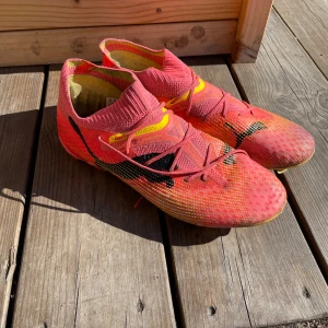 Puma Future Elite FG/AG - Säljer ett par rosa fotbollsskor från Puma med svarta detaljer och gula inslag. Skorna har snörning, stickad strumpkrage och platt sula med dobbar för bra grepp på planen. Perfekta för dig som vill sticka ut på fotbollsplanen! Elit versionen som går på både konstgräs och riktigt gräs. Växtes ut snabbt och knappt använda två månader. Kvitto från Puma kan skickas!