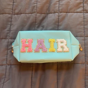 Mintgrön necessär med paljettbokstäver - Säljer en mintgrön necessär med färgglada paljettbokstäver som stavar 'HAIR' på framsidan. Väskan har dragkedja med guldfärgad detalj och är perfekt för att förvara håraccessoarer eller smink.