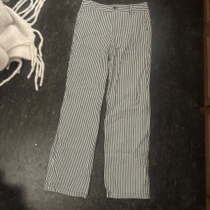 Randiga kostymbyxor från Nelly - Snygga svartvita kostymbyxor från Nelly med smala vertikala ränder. Byxorna har normal passform, bälteshällor och knappstängning i midjan. Perfekta för en stilren look och passar till många olika outfits.