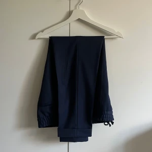 Mörkblå kostymbyxor från Filippa K - Säljer ett par mörkblå kostymbyxor från Filippa K. Byxorna har en klassisk rak passform med resår och dragsko i midjan för extra komfort. Perfekta för en stilren och avslappnad look.