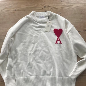 Ami Alexandre Mattiussi - Vit stickad tröja från Ami med röd hjärt- och A-detalj på bröstet. Tröjan är nästan helt ny, skicket är väldigt bra. Taggarna finns tyvärr inte längre kvar. 