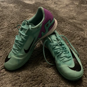 Nike inomhus fotbollsskor  - Säljer ett par turkosa Nike fotbollsskor med svarta detaljer och lila parti vid hälen. Skorna har snörning och en platt sula med greppmönster, perfekt för spel inomhus. Snygg design med stor svart Nike-logga på sidan.  Änvända väldigt sparsamt och är i grymt skick