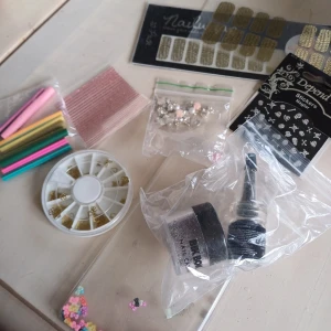 Nageldekorationer och nagelstickers mix - Ett kit med olika nageldekorationer: guldiga och svarta nagelstickers, små pärlor, strass, fimo-stavar med fruktmotiv. Perfekt för att skapa kreativa nageldesigner hemma.