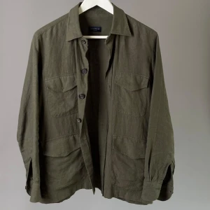 Olivgrön linneskjorta från Gaiola - Säljer en olivgrön skjorta från Gaiola i 100% linne. Skjortan har klassisk krage, fyra fickor framtill och knäppning med knappar. Perfekt för dig som gillar stilrena och avslappnade plagg med snygg passform.