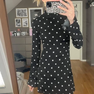 Polka dots klänning med öppen rygg - Säljer en svart kortklänning med vita prickar. Klänningen har lång ärm, hög hals och en snygg öppen rygg med stor rosett i nacken. Den e helt ny köpte den men kom alldrig till användning. POSTAR DIREKT!!!💕(den är xxs men passar xs och S LIKA bra