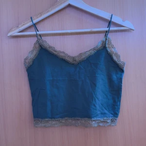 Blå croppad linnetopp med spets - Säljer en blå croppad linnetopp med tunna axelband och fina spetsdetaljer längs v-ringningen och nederkanten. Perfekt för sommardagar eller som ett lager under en skjorta.