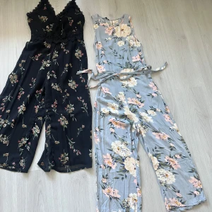 Två blommiga jumpsuits - Säljer två snygga jumpsuits med blommigt mönster. Den ena är svart med smala axelband, spets och v-ringning, medan den andra är ljusblå med stora blommor och tillhörande knytband i midjan. Perfekta för sommarens alla tillfällen!