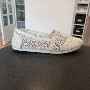TOMS Alpargata Classic Morrocan  - Säljer ett par vita ballerinaskor från TOMS med vackert blommigt spetsmönster. Skorna är i fint skick och har bara använts ute vid ett tillfälle i 10 minuter, men kommer inte till användning på grund av fel storlek. NYPRIS: 500kr🌸👟