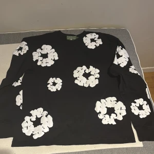 Denim Tears hoodie - Säljer en svart långärmad tröja från Denim Tears med stora vita blommor tryckta över hela tröjan. Tröjan har en klassisk passform och är tillverkad i mjuk bomull. Perfekt för dig som vill sticka ut med en unik design. ⚠️1:1⚠️