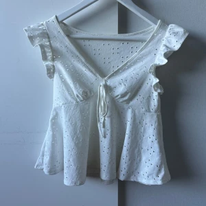 Vit blus med volangärmar - Säljer en supersöt sommartopp med rosett man kan knyta vid bysten och lite volanger vid axlarna 