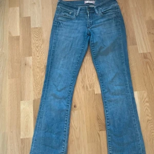 Blå bootcut jeans med broderade bakfickor - Säljer ett par klassiska blå jeans med bootcut passform. Jeansen har fem fickor, dragkedja och knapp framtill samt snygga broderade detaljer på bakfickorna. Perfekta till vardags och lätta att matcha med olika toppar.