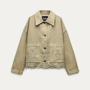 Beige jacka med broderade detaljer från Zara - Säljer en beige jacka från Zara med fina broderade blommor och hålmönster längs nederkanten och på fickorna. Jackan har krage, knappar framtill och två stora fickor. Perfekt för dig som gillar unika detaljer!