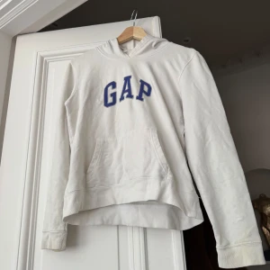 Vit hoodie från GAP - Säljer en klassisk vit hoodie från GAP med blå broderad logga på bröstet. Den är lite tunnare material än vanliga hoodies och passar perfekt som sommartröja. 