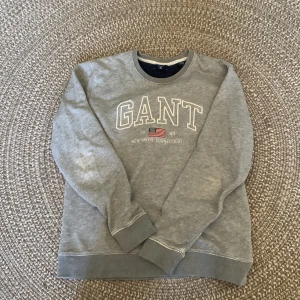 Grå GANT sweatshirt - Säljer nu en grå sweatshirt från GANT. Skick 7/10 pga lite slitage på armbåge. Se slitaget på bild 3. Perfekt för en mer avlsappnad stil. Pris kan diskuteras. Frakten står inte med i priset!!!