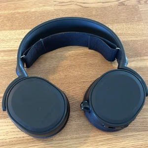Svarta hörlurar från SteelSeries med sladd - Säljer ett par svarta over-ear hörlurar från SteelSeries med mjuka öronkuddar och justerbart huvudband. Hörlurarna har inbyggda knappar för volym och mikrofon samt uttag för ljudkabel. Perfekta för gaming eller musik.