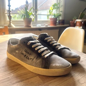 Grå sneakers från Saint Laurent - Säljer dessa par grå sneakers från Saint Laurent Skorna har en handskriven logga på sidan och är i mycket bra skick! Dessa är otroligt svåra att få tag på då de inte säljs längre. Nypris låg förut på  runt 7-8. MITT PRIS 5000. Dustbag följer med!