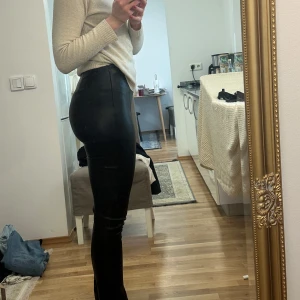 Byxor i skinnimitation med slits - Svarta byxor från Gina i skinnimktation, långa ben, hög midja och slits längst ned! Använda sparsamt, max 2-3ggr! 