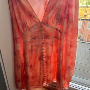 Rosa blommig långklänning från Adoore - Säljer en klänning från Adoore i rosa toner med blommigt mönster. Klänningen har v-ringning, långa ärmar och dekorativa knappar framtill. Perfekt för sommarens alla tillfällen!