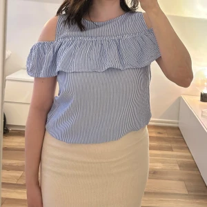 Blåvit offshoulder blus från H&M st 170 - Säljer en blåvit randig blus från H&M med offshoulder-design och volangdetalj över bröstet. Blusen har smala axelband och är tillverkad i ett lätt bomullsmaterial. Perfekt för varma dagar. Storlek 170.