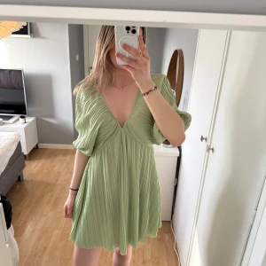 Ljusgrön plisserad kortklänning med v-ringning - Superfin ljusgrön kortklänning med plisserat tyg och djup v-ringning. Klänningen har vida, korta ärmar och en flowy passform som ger en luftig känsla. Perfekt för varma dagar och somriga tillfällen. Superfint skick!💕