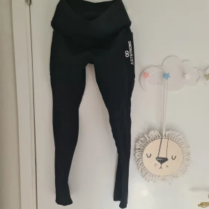 Svarta träningstights från Just Strong S  - Svarta tights från Just Strong med logga på benet. De är tighta och har hög midja, perfekta för träning eller gym. Gjorda i stretchigt syntetmaterial som sitter skönt och följsamt. Det finns två rymliga fickor på båda sidorna , perfekt för att förvara gymkort eller mobil. Mycket bra skick ny pris ca 800 kr. 