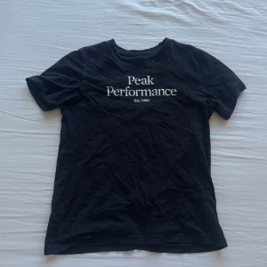 Svart t-shirt från Peak Performance - Säljer en svart t-shirt från Peak Performance med vit logga och text 'Est. 1986' på bröstet. Klassisk rund halsringning och korta ärmar. Perfekt för en stilren och enkel look.