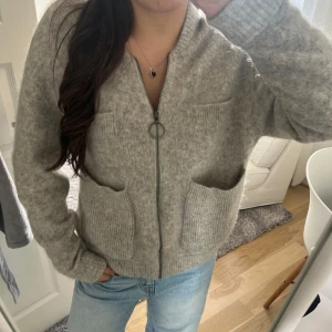 Grå stickad kofta med dragkedja - Mysig grå stickad kofta med dragkedja och två stora fickor framtill. Koftan har långa ärmar och en avslappnad passform, perfekt för lager-på-lager. Passar till det mesta och är superenkel att styla. Koftan är i äkta mohair!