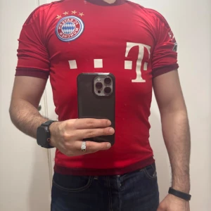 Röd Bayern München fotbollströja - Säljer en röd Bayern München fotbollströja med vita detaljer och klubbmärke på bröstet. Tröjan har korta ärmar och klassisk passform. Perfekt för dig som vill visa ditt stöd för laget.