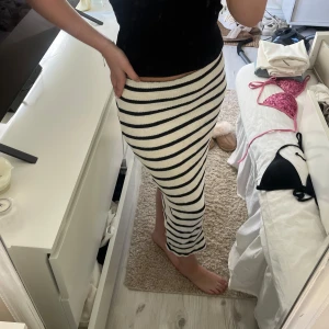  stickad långkjol - Säljer en vit stickad långkjol med svarta horisontella ränder. Kjolen har en tight passform och en liten slits på sidan. Perfekt för dig som gillar en enkel men snygg stil.