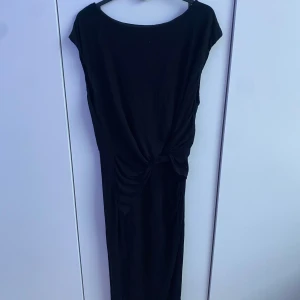 Svart långklänning från H&M - Säljer en svart långklänning från H&M i storlek 40. Klänningen har rund halsringning, korta ärmar och en snygg knutdetalj i midjan som ger en smickrande siluett. Perfekt för dig som gillar stilrena och enkla plagg.