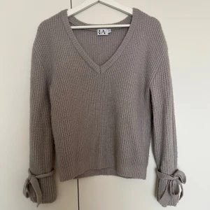 Ljusgrå stickad tröja  - Supermjuk ljusgrå stickad tröja med v-ringning och långa ärmar. Ärmarna har snygga knytband vid handlederna som ger en extra detalj. Passar XS/S