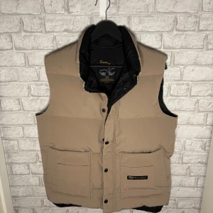 Canada Goose väst - Säljer en beige dunväst från Canada Goose med svart innerfoder. Västen har två stora fickor framtill och stängs med både knappar och dragkedja. Nypris runt 6000kr. Hör av dig vid intresse 🙌