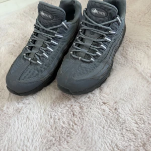 Grå Nike Air Max sneakers - Säljer ett par grå Nike Air Max sneakers med mesh och syntetdetaljer. Skorna har snörning, rund tå och en platt sula med synlig Air Max-dämpning. Perfekta för dig som gillar sportig stil och vill ha bekväma skor till vardags.