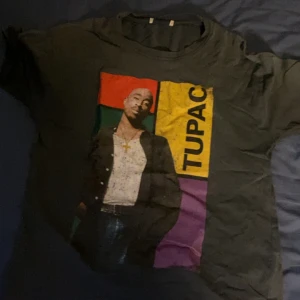 Svart T-shirt med Tupac-tryck - Cool svart T-shirt med stort färgglatt tryck av Tupac på framsidan. T-shirten har klassisk passform och korta ärmar. Perfekt för dig som gillar streetwear och vill sticka ut med en ikonisk look.