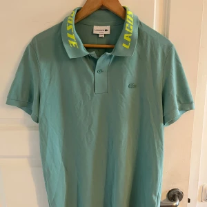 Mintgrön pikétröja från Lacoste med gul logga på kragen - Säljer en mintgrön pikétröja från Lacoste i slim fit-modell. Kragen har stor gul Lacoste-logga och tröjan har klassisk knappslå framtill. Perfekt för en sportig och stilren look. Limited edition skjorta också går ej o hitta någonstans, köpt utomlands 