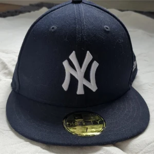 Mörkblå New Era Yankees keps - Säljer en mörkblå New Era 59FIFTY keps med New York Yankees-logga framtill. Kepsen har rak skärm och broderade detaljer, samt MLB-logga baktill. Storlek 7 (55,8 cm). Perfekt för dig som gillar sportig stil.