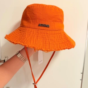 Jacquemus bucket hat - Säljer en helt ny och oanvänd Jacquemus solhatt i orange färg. Trendigt bred brätte med fransad kant och justerbart hakband – perfekt för sommaren! Äkta vara med metallogo framtill.  Skicka PM vid intresse!